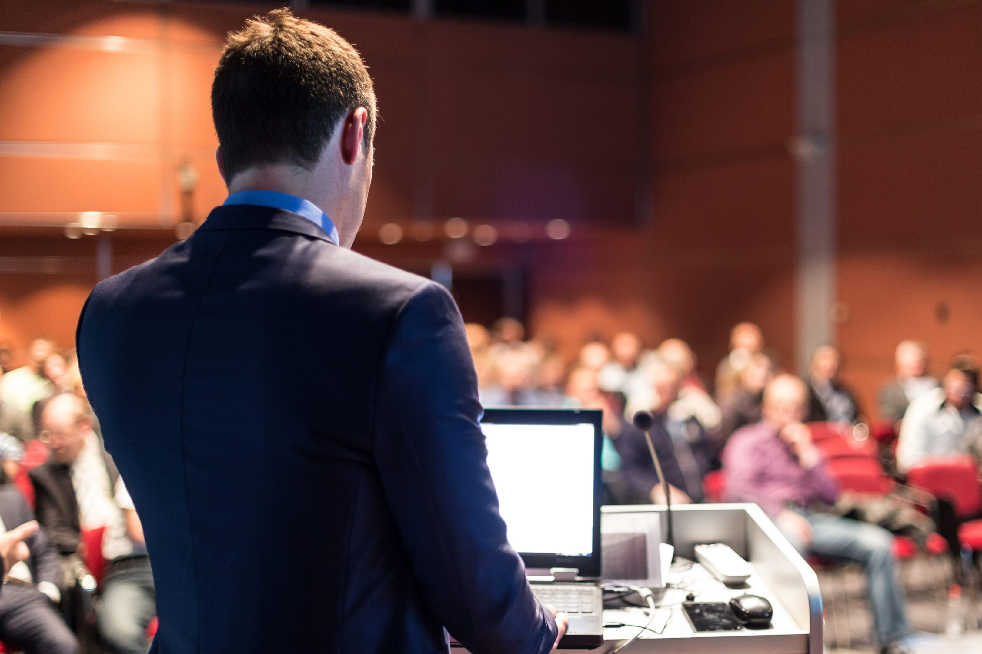 Man at podium, blurred audience